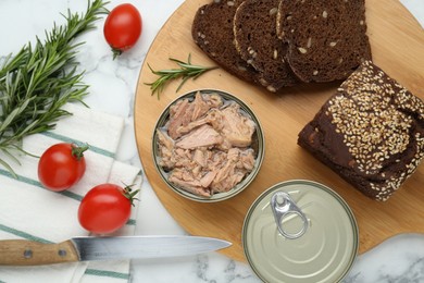 Tin cans with canned tuna and products on white marble table, flat lay