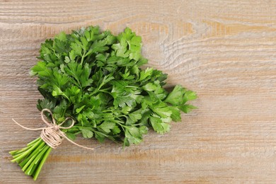 Photo of Bunch of fresh green parsley leaves on light wooden table, top view. Space for text