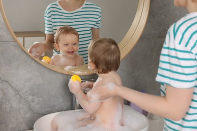 Mother washing her little baby in sink indoors