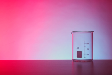 Photo of Empty beaker on table against color background. Chemistry laboratory glassware