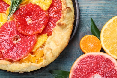 Photo of Delicious galette with citrus fruits and rosemary on blue wooden table, flat lay