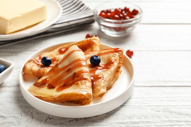 Thin pancakes served with syrup and berries on plate