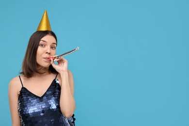 Photo of Happy young woman in party hat with blower on light blue background