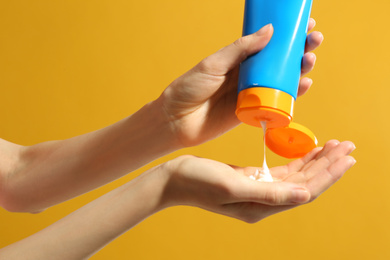 Photo of Woman applying sun protection cream on hand against yellow background, closeup
