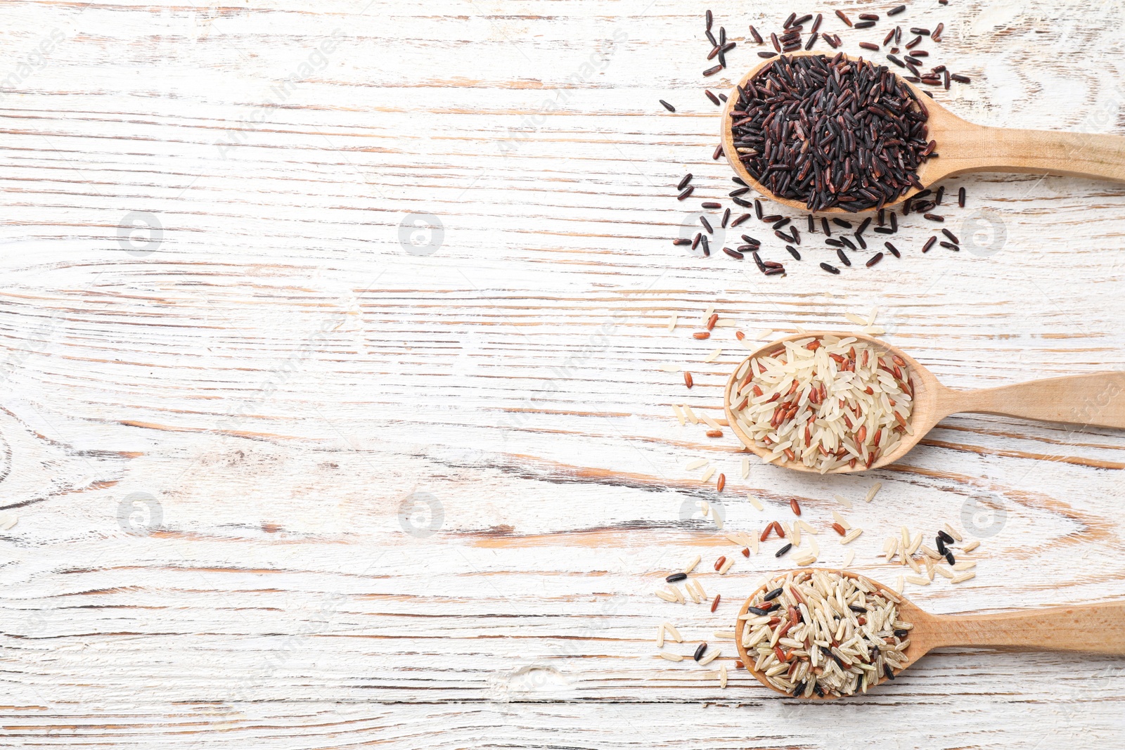 Photo of Different sorts of rice on white wooden table, flat lay. Space for text