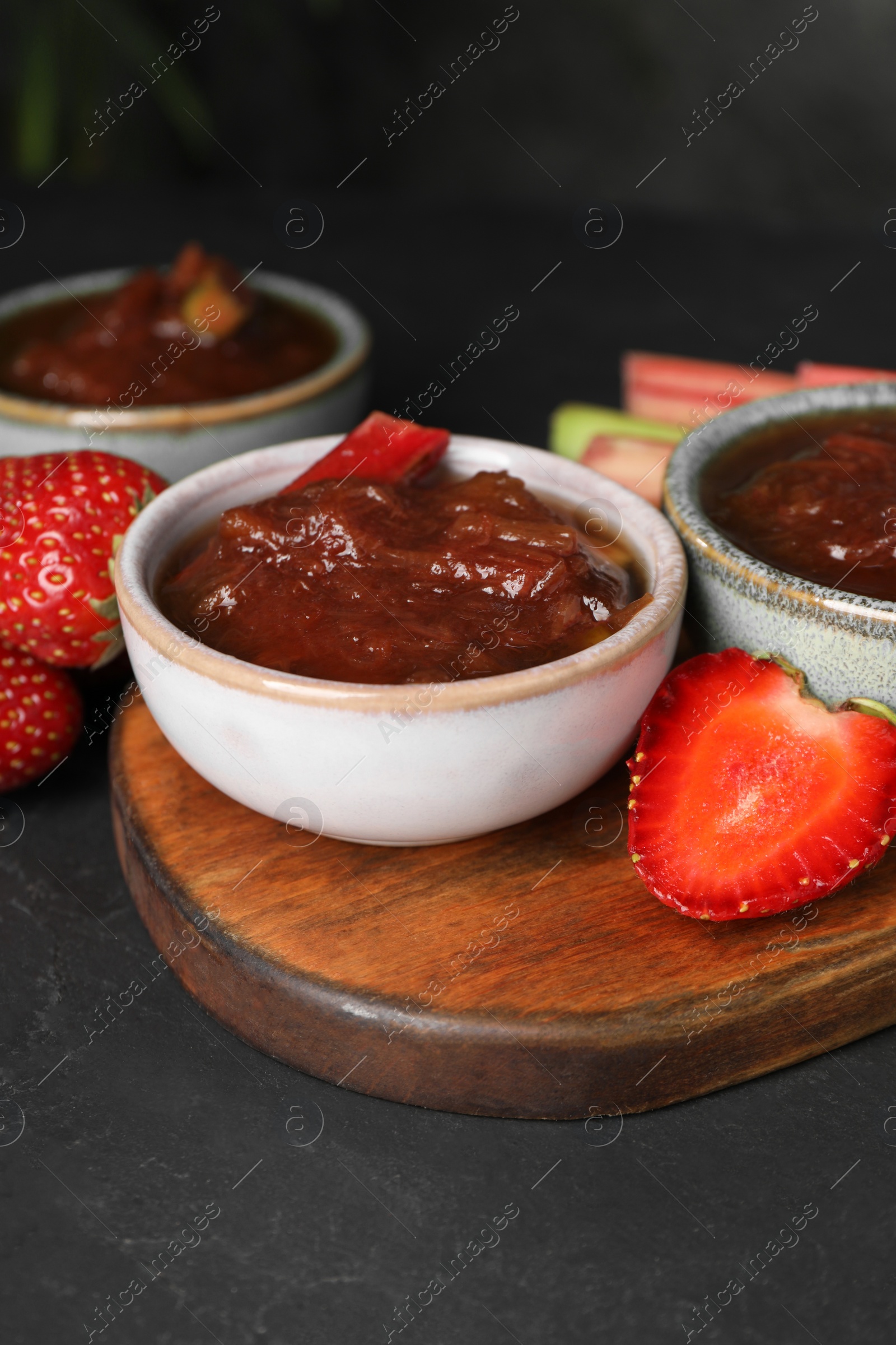 Photo of Tasty rhubarb jam in bowls and strawberries on dark table