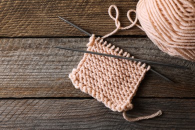 Soft beige yarn, knitting and metal needles on wooden table, flat lay. Space for text