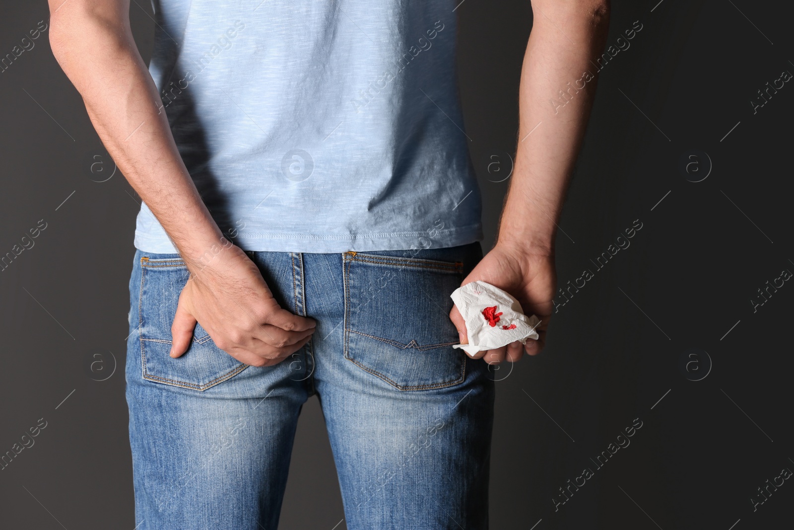 Photo of Man holding toilet paper with blood stain on black background, closeup. Hemorrhoid concept