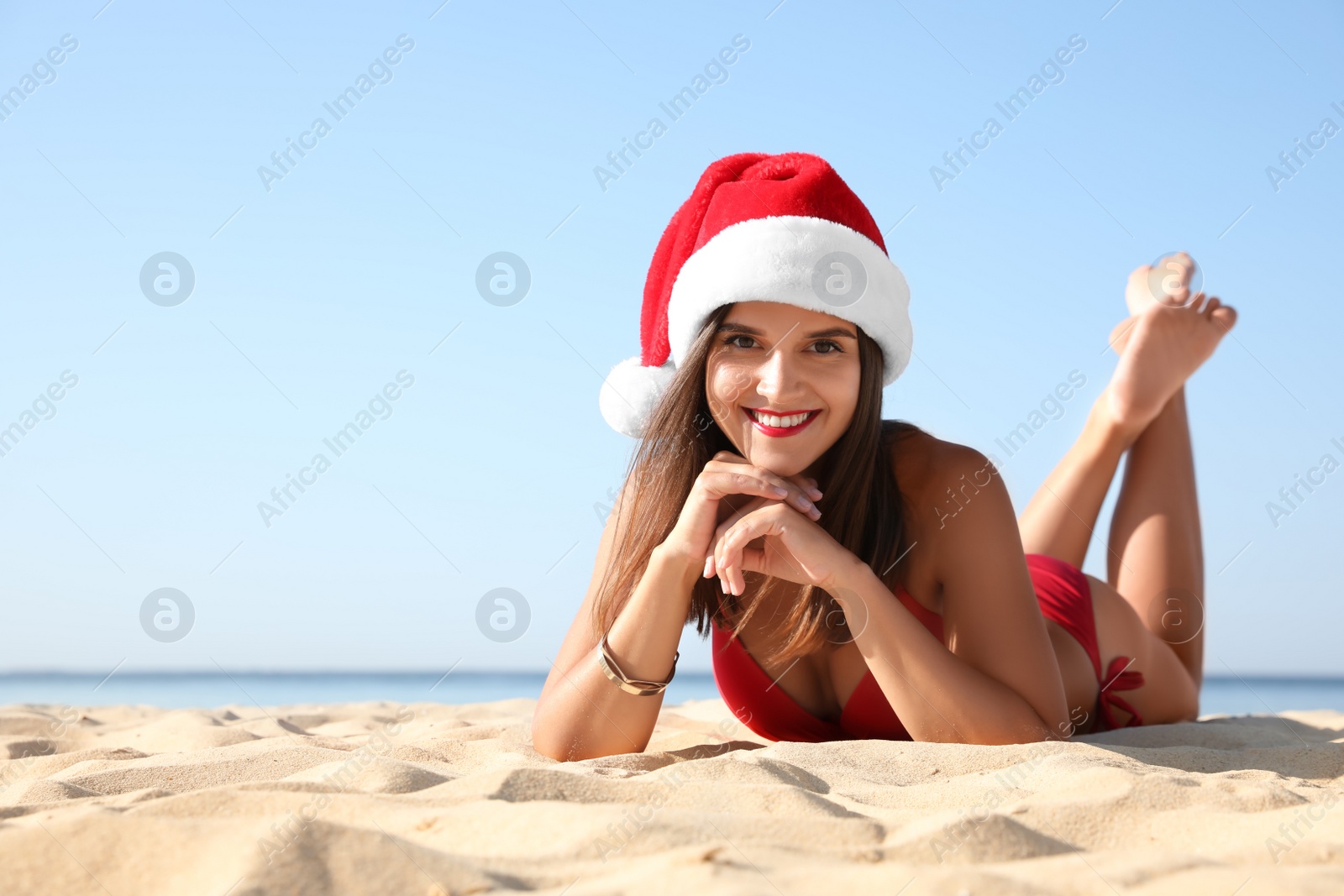 Photo of Young woman wearing Santa hat and bikini on beach, space for text. Christmas vacation