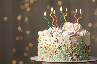 Photo of Beautiful birthday cake with burning candles on stand against festive lights. Space for text