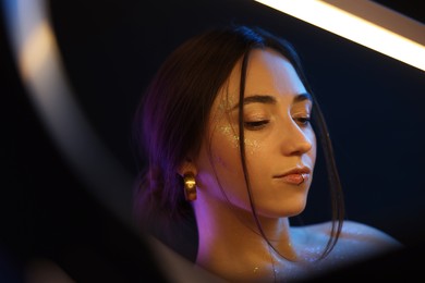 Portrait of beautiful woman on dark background in neon lights, view through ring lamp