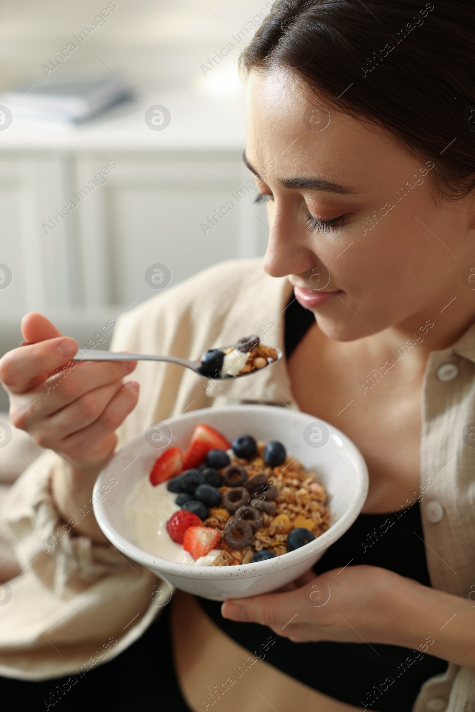 Photo of Woman eating tasty granola with fresh berries and yogurt at home, closeup