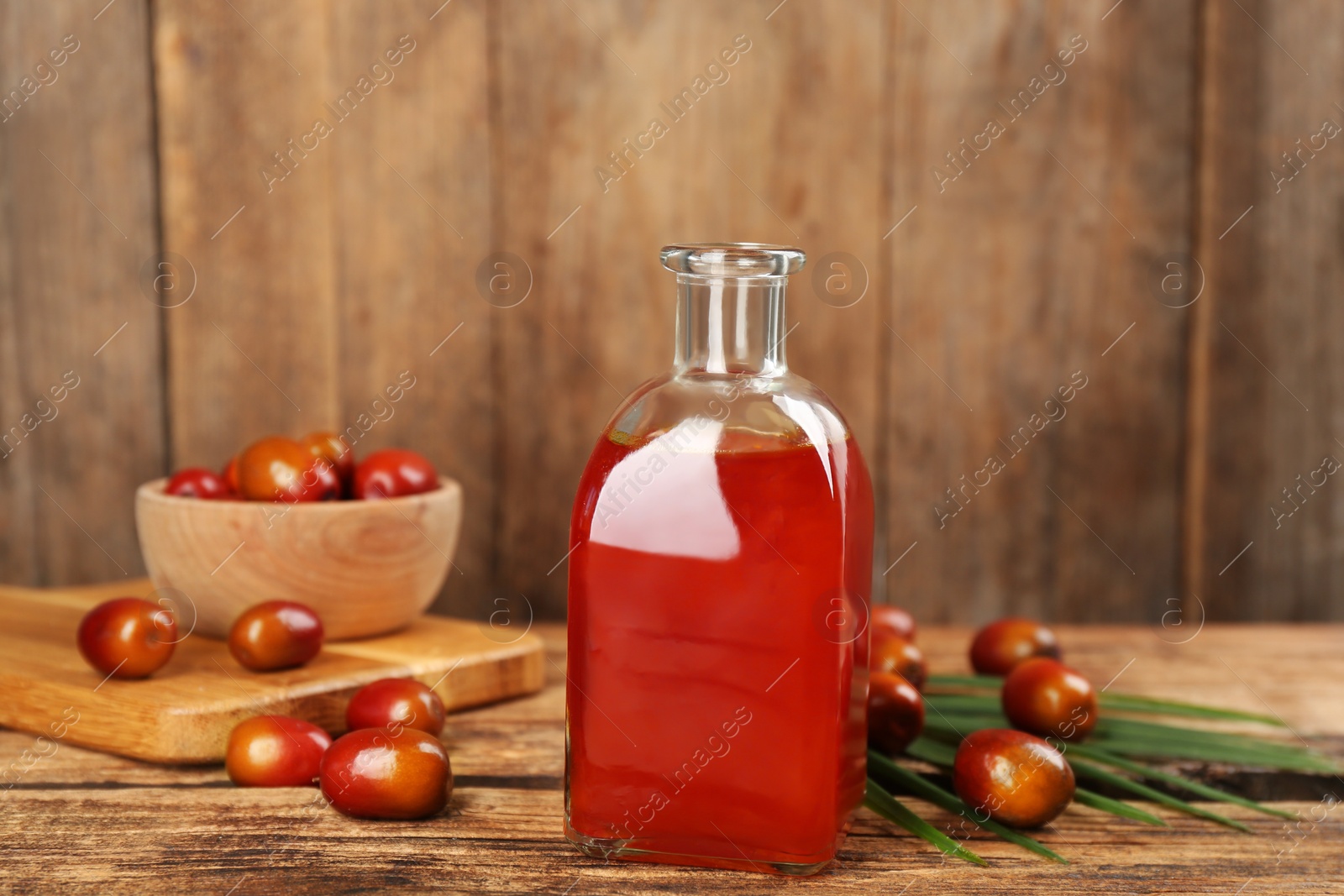 Photo of Palm oil in glass bottle, tropical leaf and fruits on wooden table