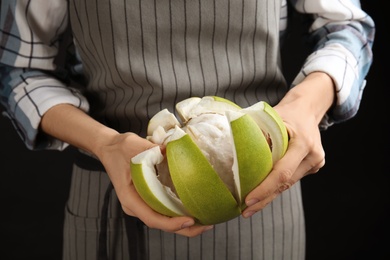 Photo of Woman peeling fresh ripe pomelo on black background, closeup