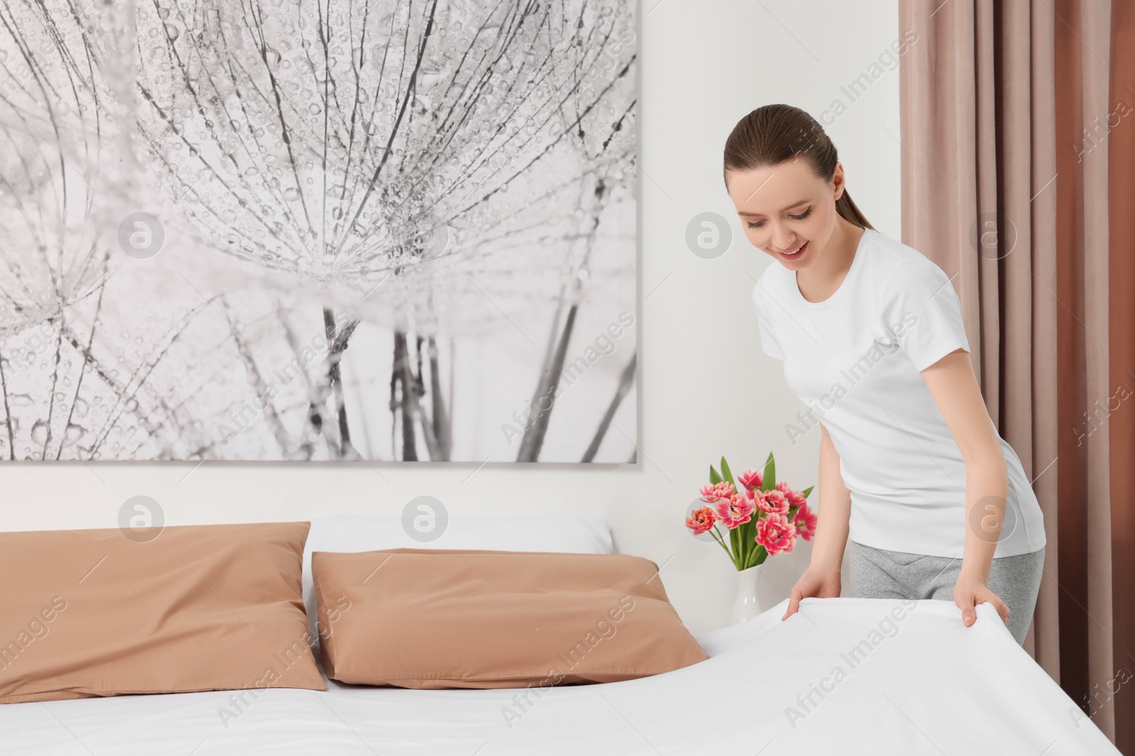 Photo of Young woman making bed in room. Space for text