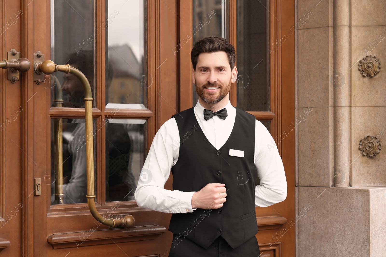 Photo of Butler in elegant suit near wooden hotel door. Space for text