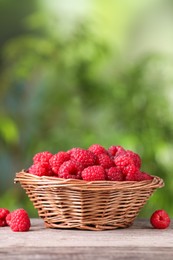 Photo of Wicker basket with tasty ripe raspberries on wooden table against blurred green background, space for text