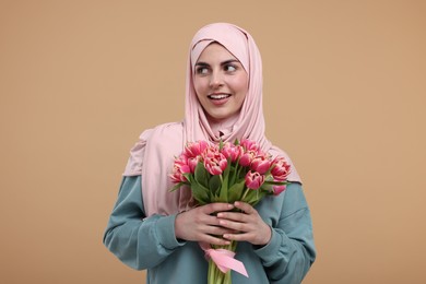 Happy woman in hijab with beautiful bouquet on beige background