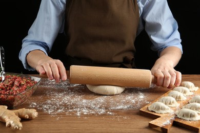 Photo of Woman rolling dough for gyoza at wooden table, closeup