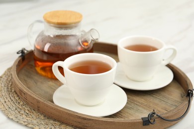 Photo of Aromatic tea in cups and teapot on white table, closeup