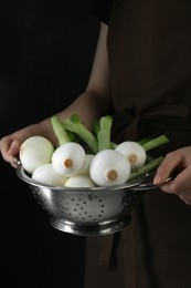 Photo of Woman holding colander with green spring onions on black background, closeup
