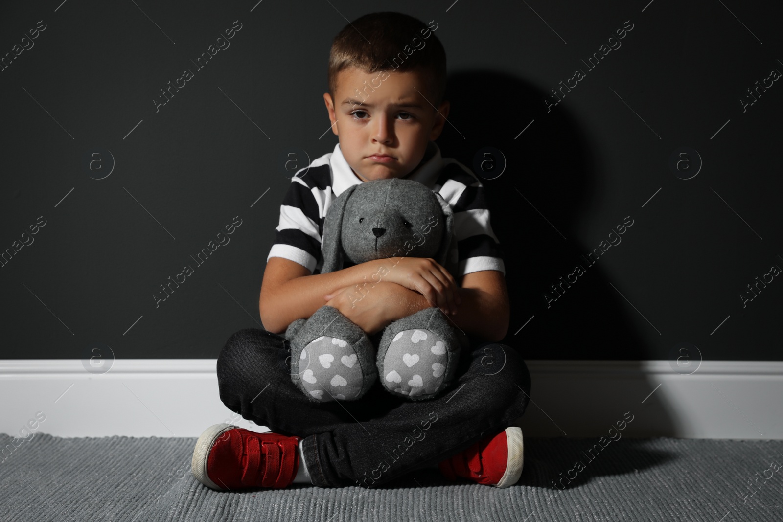 Photo of Sad little boy with toy near black wall. Domestic violence concept