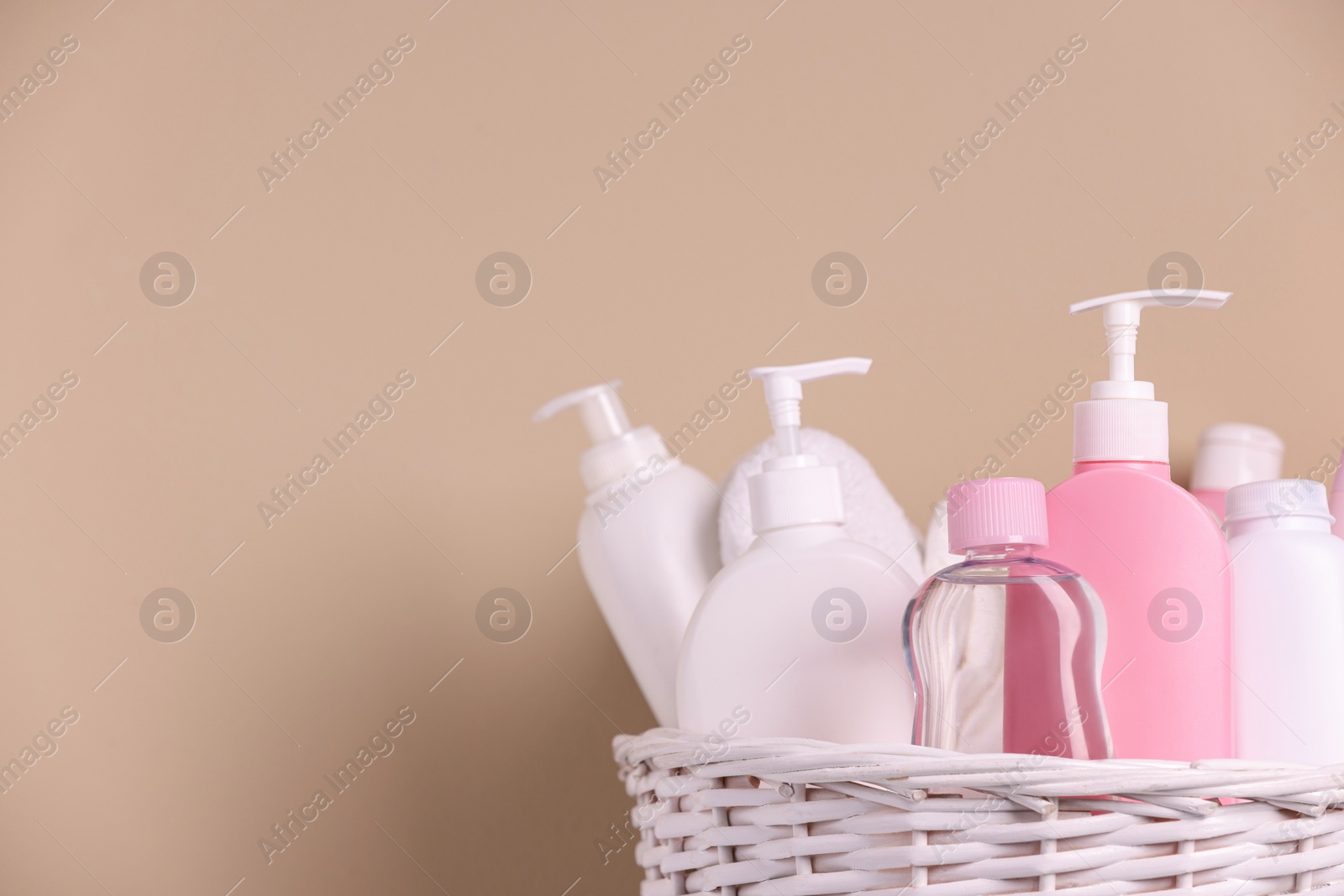 Photo of Baby cosmetic products in wicker basket on beige background, closeup. Space for text