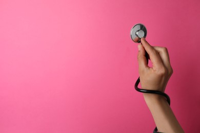 Photo of Woman holding stethoscope on pink background, closeup. Space for text