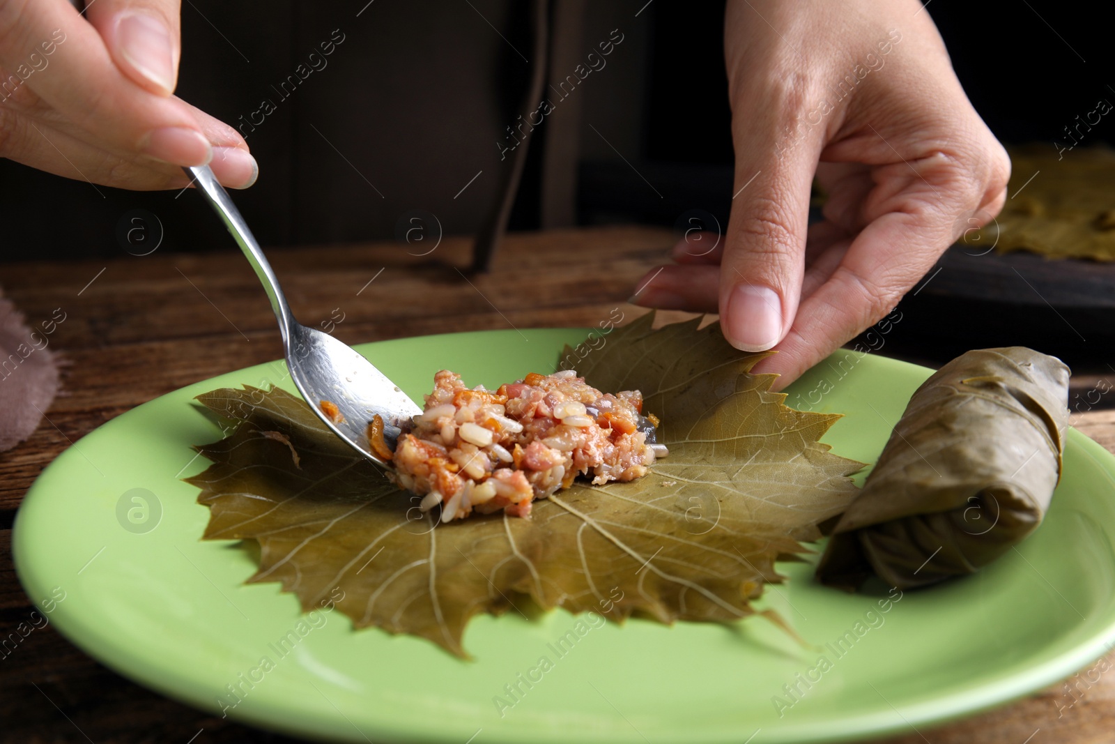 Photo of Woman preparing stuffed grape leaves on plate, closeup