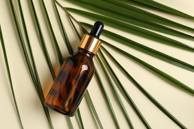 Photo of Bottle with cosmetic oil and green leaf on beige background, top view