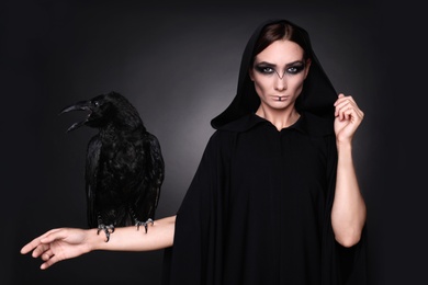Photo of Mysterious witch with raven on dark background