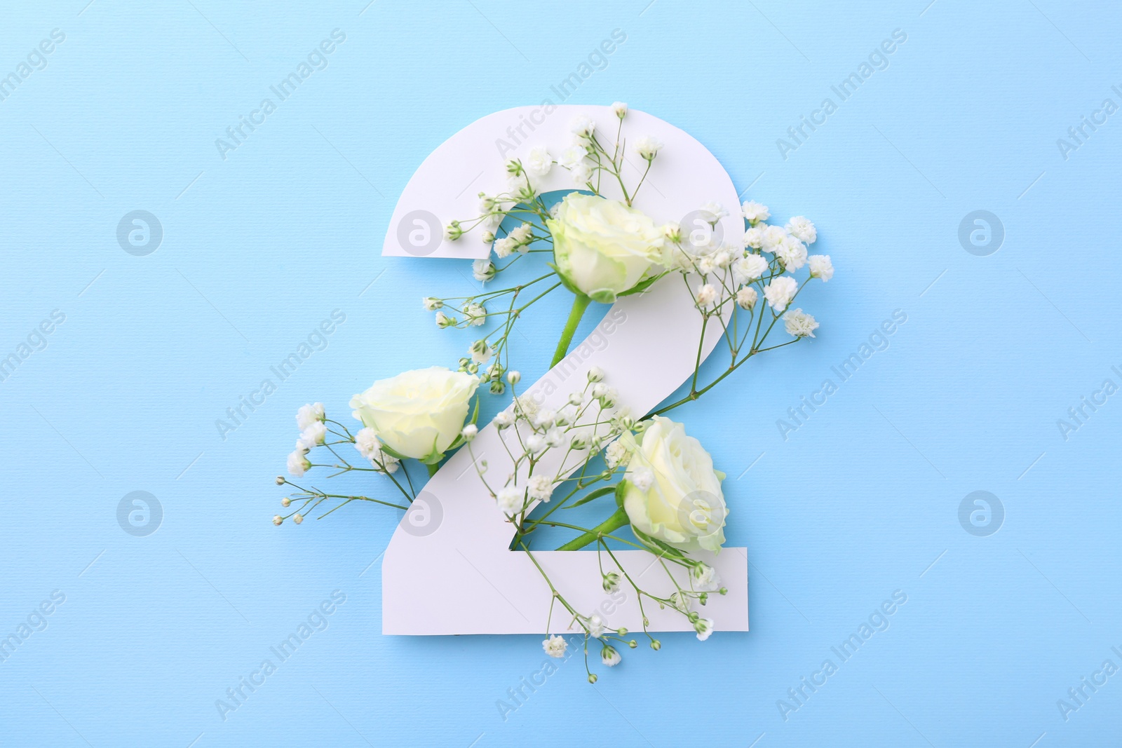 Photo of Paper number 2 and beautiful flowers on light blue background, top view