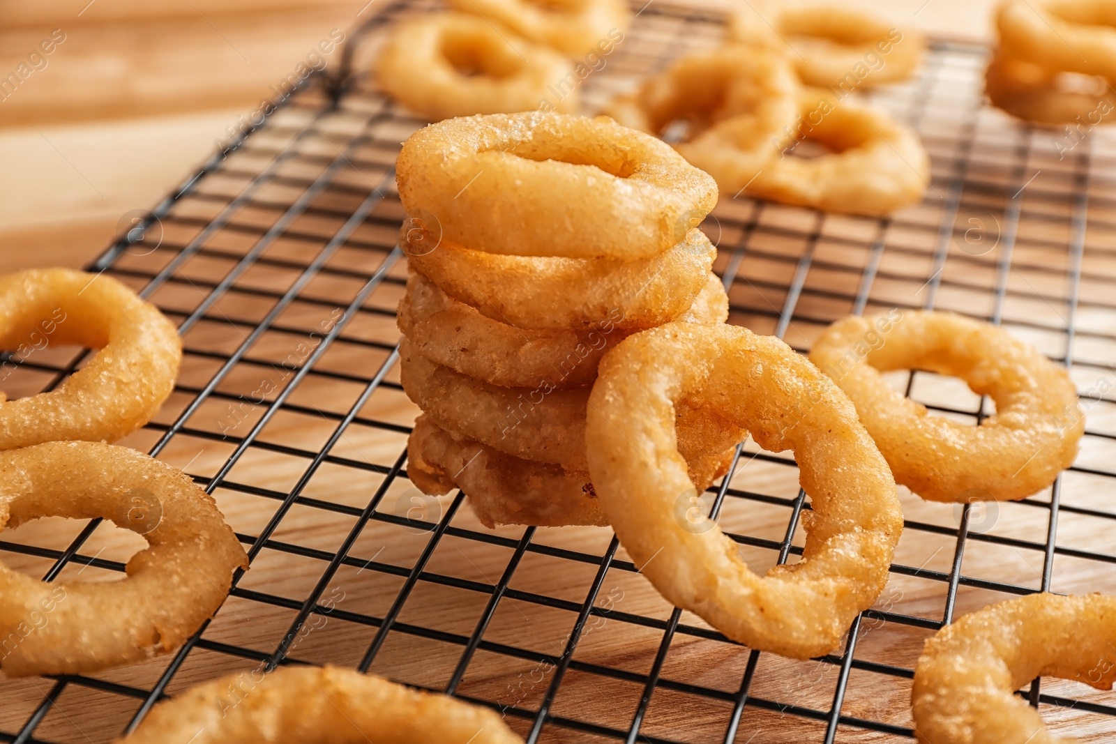 Photo of Cooling rack with tasty onion rings on table, closeup