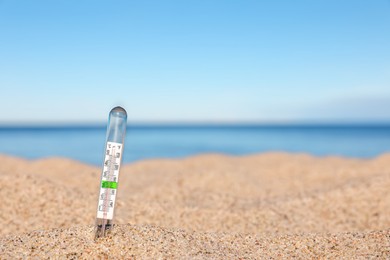 Weather thermometer in sand near sea, space for text