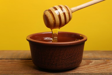 Pouring honey from dipper into bowl at wooden table against golden background