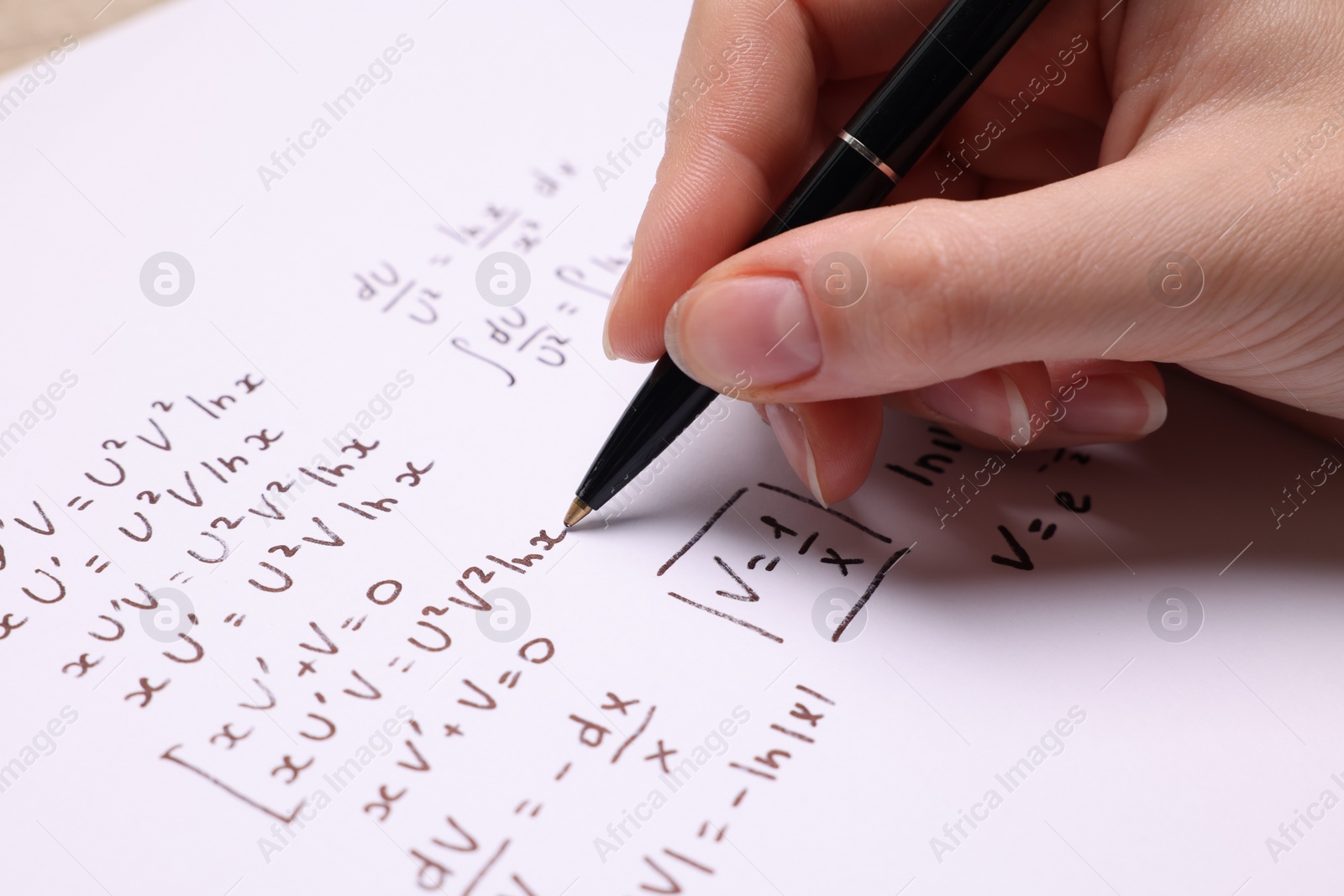 Photo of Student writing different mathematical formulas on paper, closeup