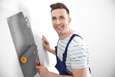 Young male decorator painting wall in room