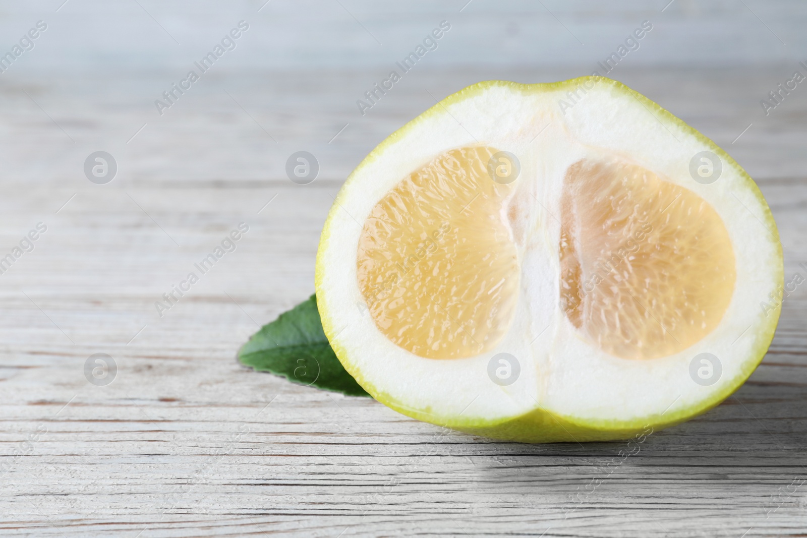Photo of Half of sweetie fruit on white wooden table, space for text