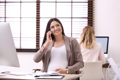 Photo of Young pregnant woman talking on phone while working in office