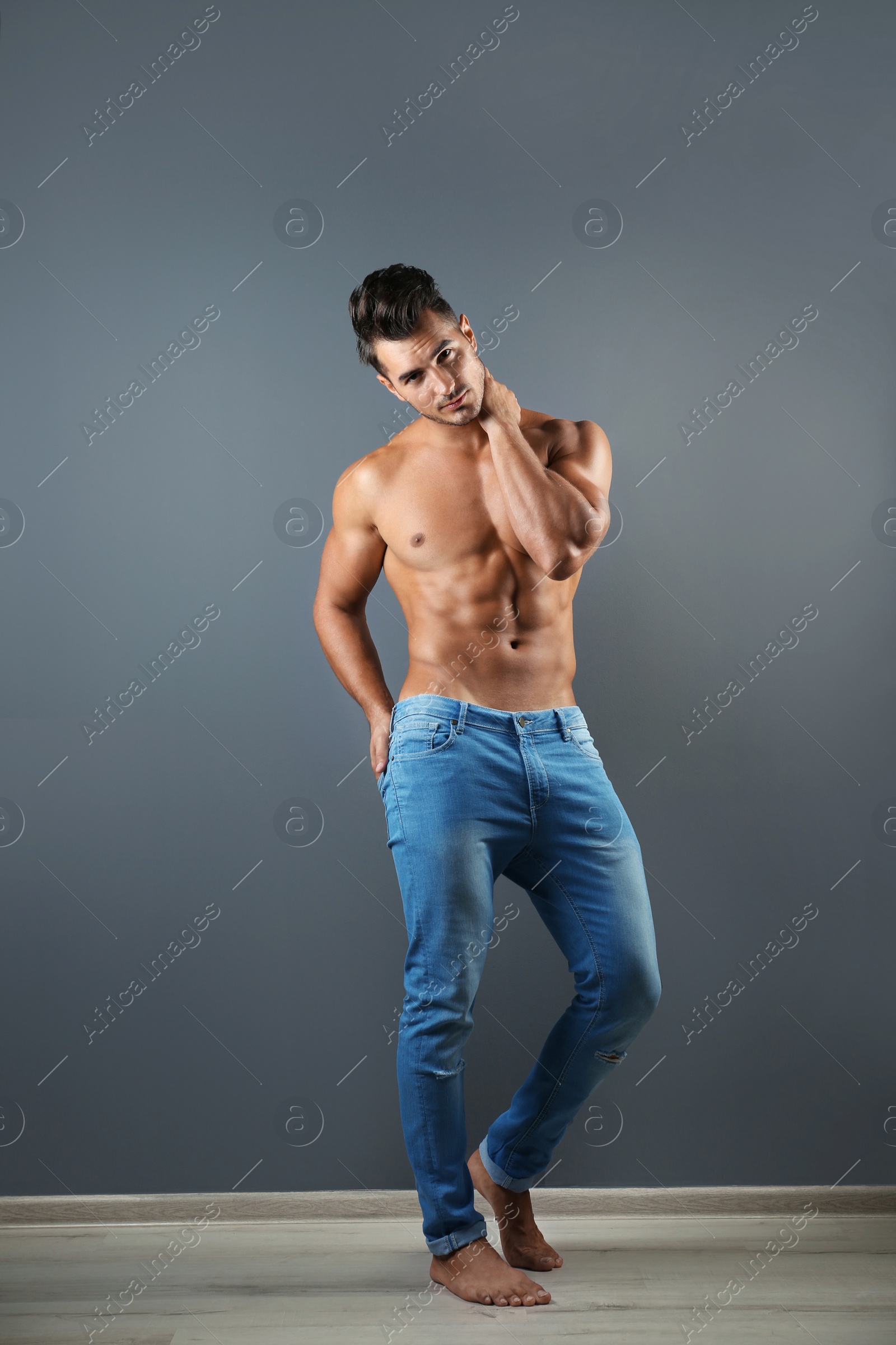 Photo of Shirtless young man in stylish jeans near grey wall