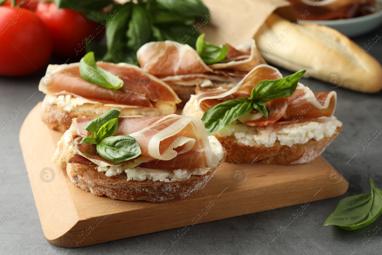 Photo of Tasty sandwiches with cured ham and basil on grey table, closeup
