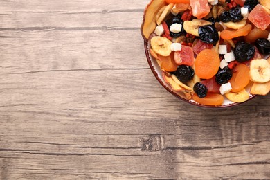 Photo of Bowl with different tasty dried fruits on wooden table, top view. Space for text