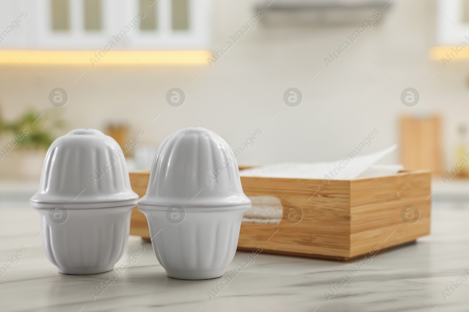 Photo of Ceramic salt and pepper shakers near box of napkins on white marble table in kitchen. Space for text