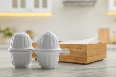 Ceramic salt and pepper shakers near box of napkins on white marble table in kitchen. Space for text