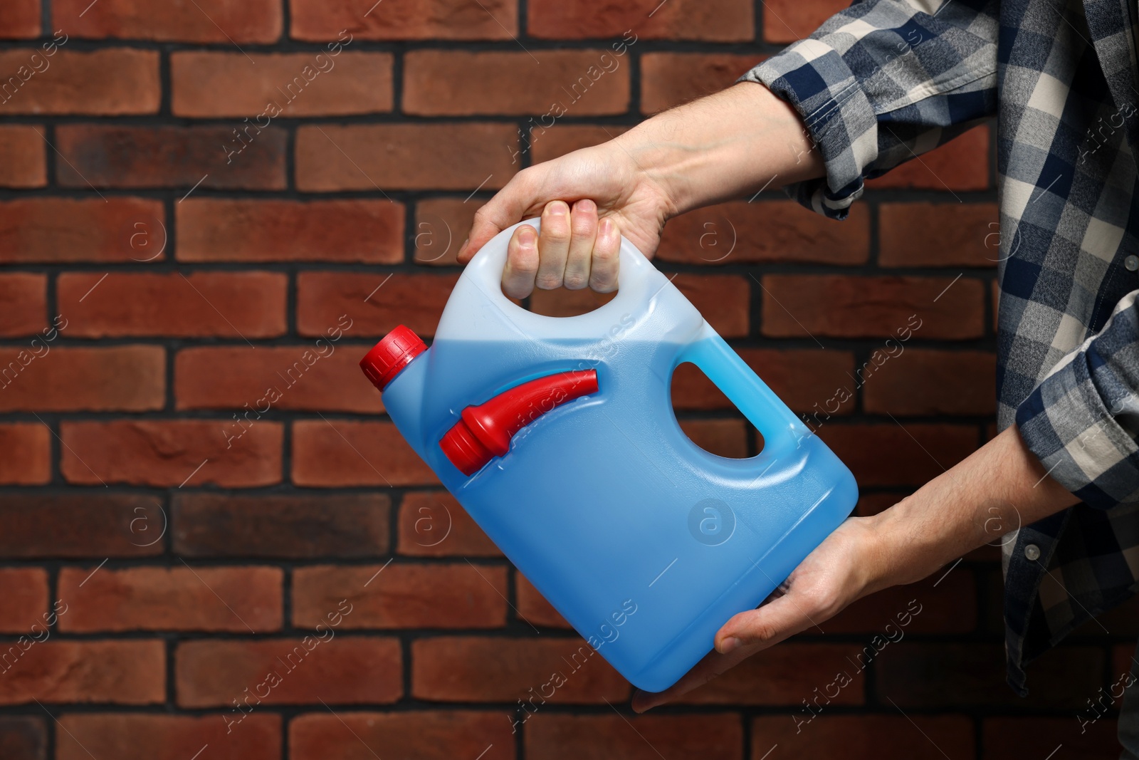 Photo of Man holding canister with blue liquid near brick wall, closeup. Space for text