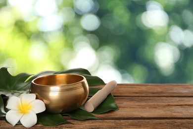 Image of Golden singing bowl, mallet, leaf and flower on wooden table outdoors, space for text