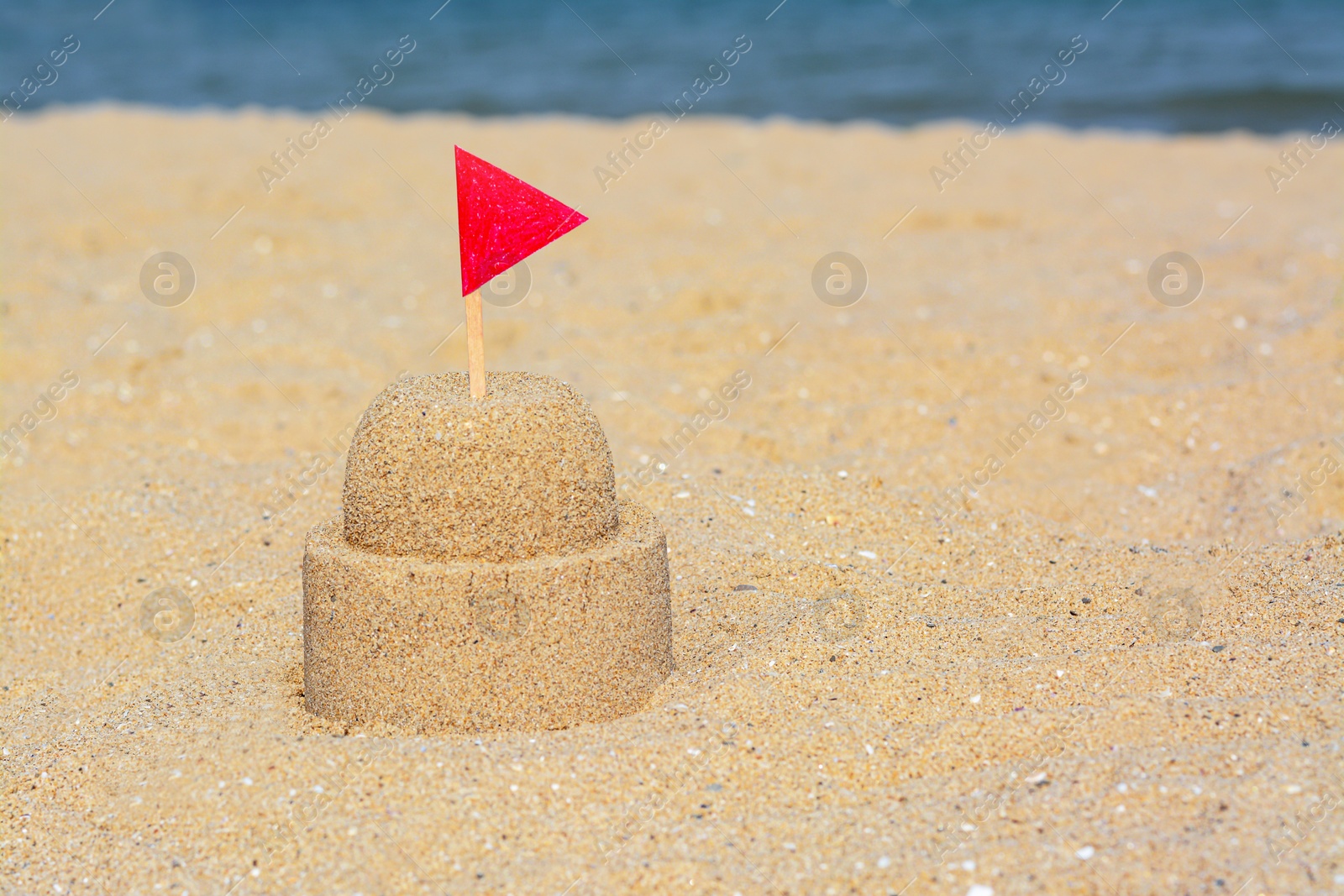 Photo of Beautiful sand castle with red flag on beach, space for text