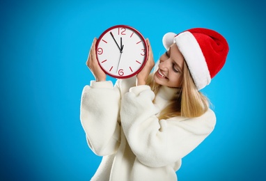 Woman in Santa hat with clock on light blue background. New Year countdown