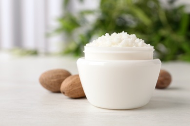 Jar of shea butter and nuts on table against blurred background. Space for text