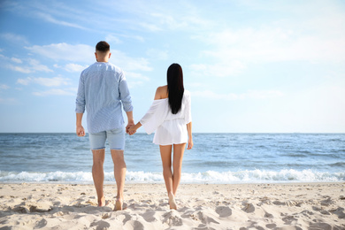 Photo of Lovely young couple walking together on beach, back view